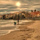 Surfer walking on beach at sunset with buildings and dramatic clouds