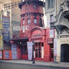 Whimsical Parisian street with Moulin Rouge windmill, vintage car, and glowing store fronts