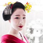 Digital artwork of geisha with white makeup and golden fan on floral background