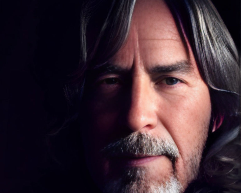 Detailed portrait of man with long gray hair and goatee, half face in light, half in shadow