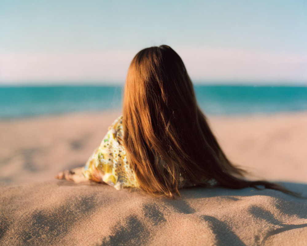 Long-Haired Person Sitting on Sandy Beach Facing Tranquil Sea