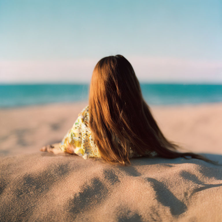 Long-Haired Person Sitting on Sandy Beach Facing Tranquil Sea