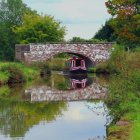 Tranquil river scene with colorful reflections of buildings, greenery, boats, and people