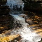 Cascading Waterfall Over Layered Rock Formations & Turbulent Pool