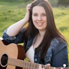 Portrait of young woman with curly hair and guitar in nature setting