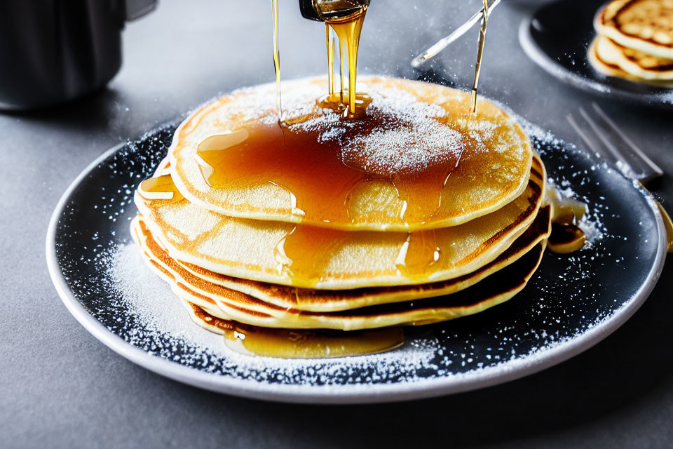 Golden pancakes with butter, syrup, and powdered sugar on white plate