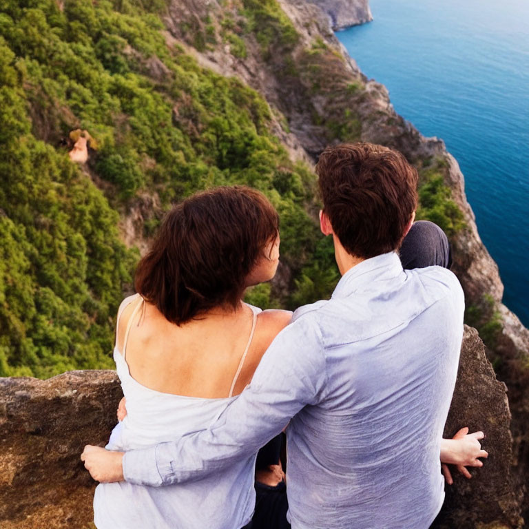 Couple sitting on scenic cliff with lush greenery and blue sea