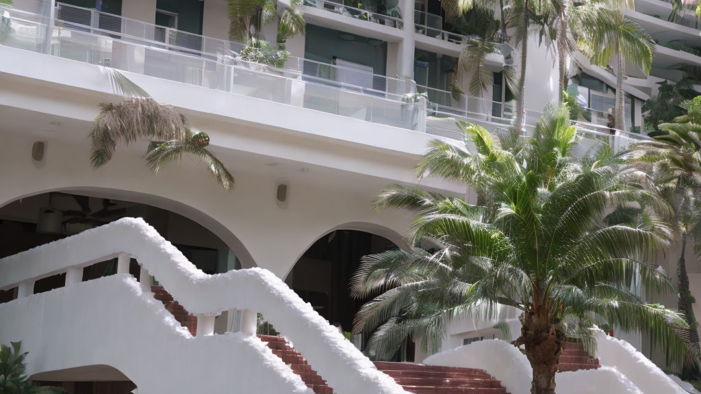 Modern building with white arches and staircases in lush green palm tree setting