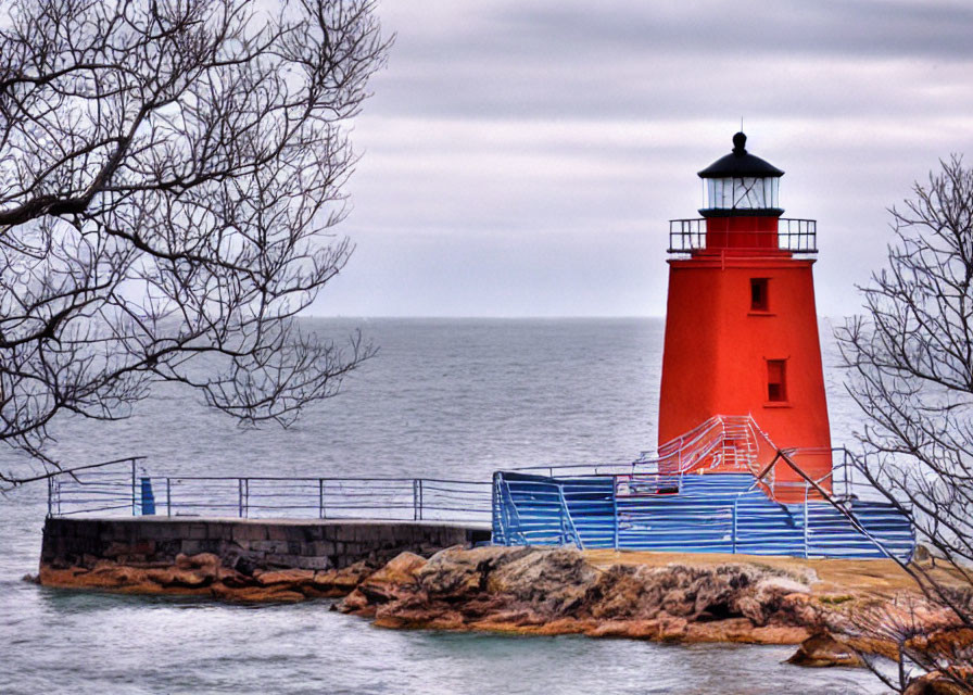 Red lighthouse on rocky outcrop with trees and blue railing by the sea