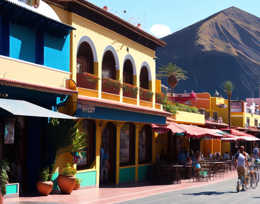 Vibrant buildings with arched doorways and outdoor seating under clear blue sky with volcano.