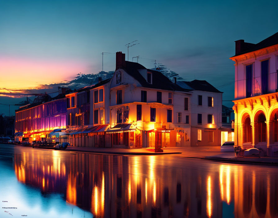 Tranquil waterway at twilight with illuminated buildings and vivid sunset sky.