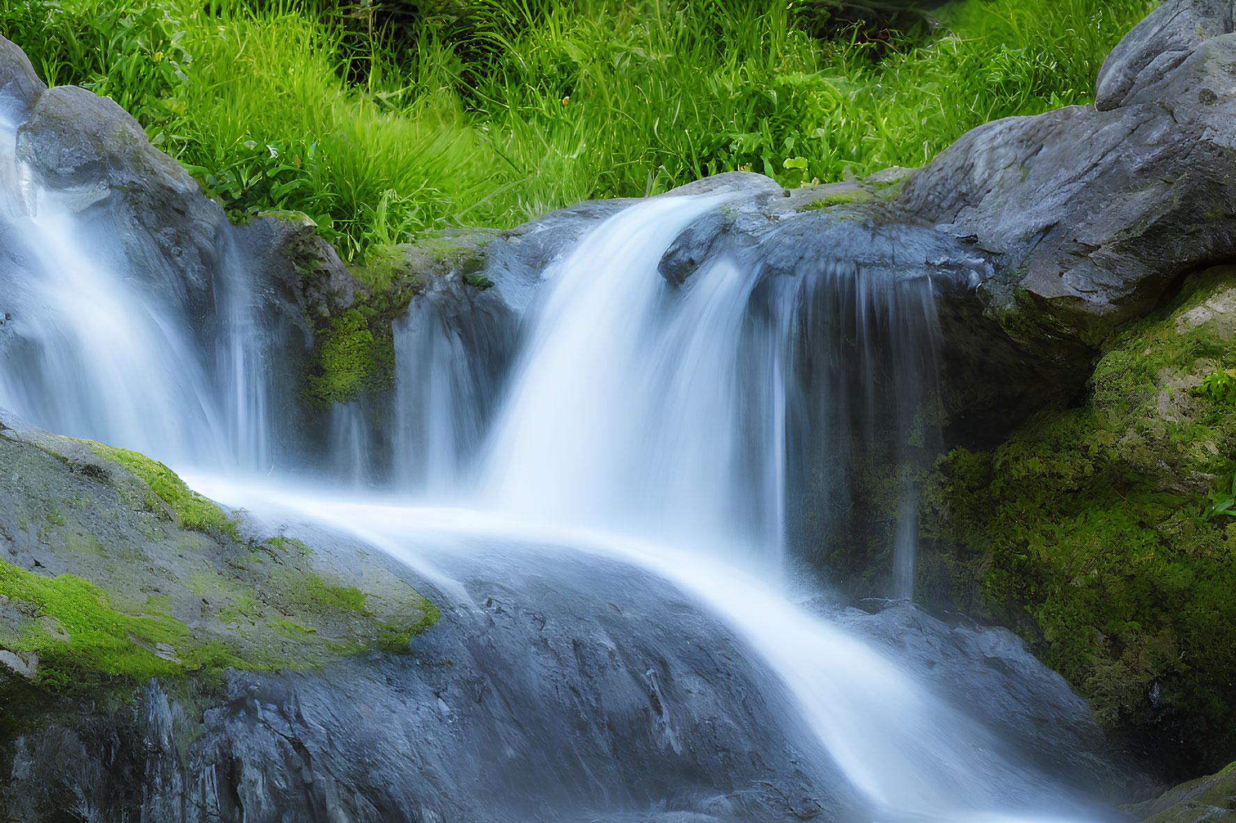 Tranquil waterfall over mossy rocks in lush green setting