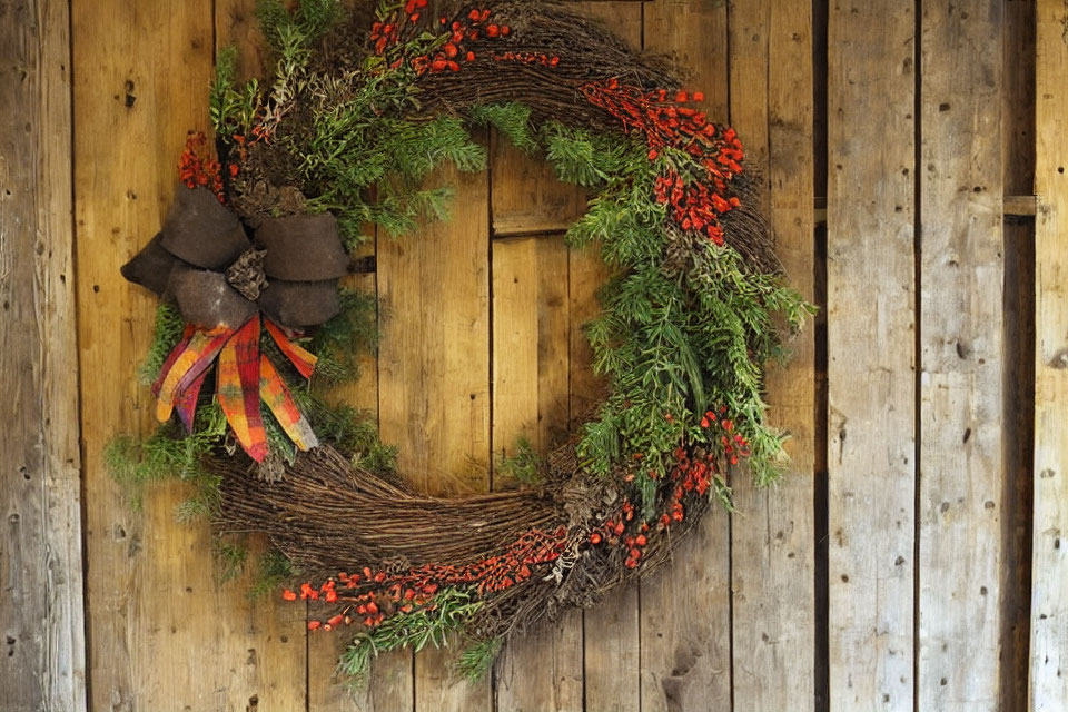 Festive wreath with red berries and green foliage on textured wooden wall