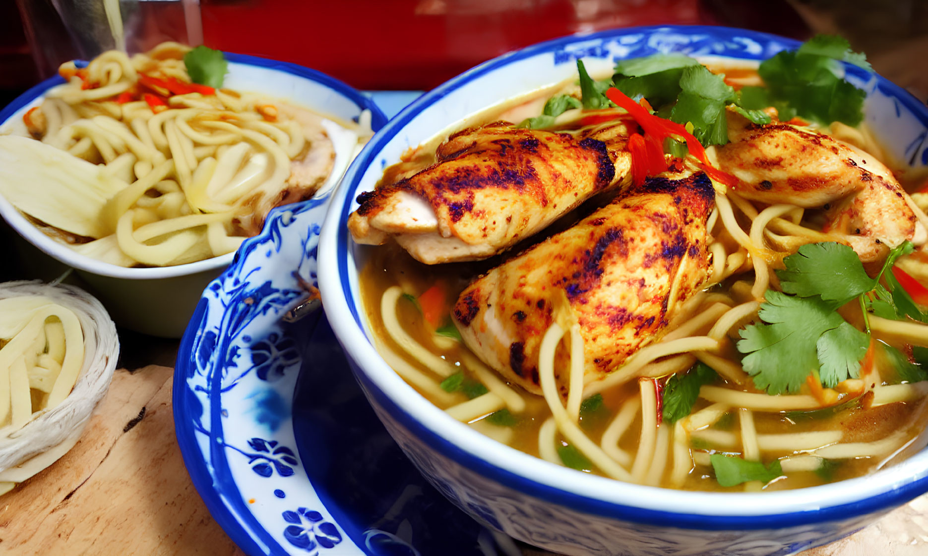 Asian noodle soup with grilled chicken, cilantro, and red pepper in a blue patterned bowl