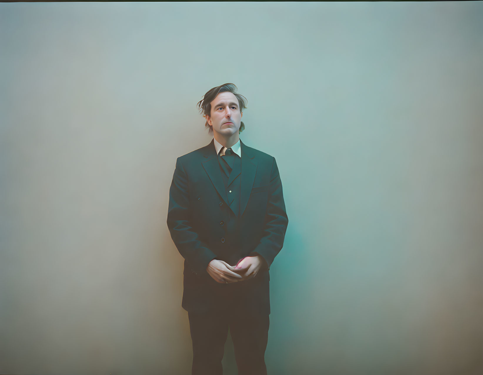 Pensive man in dark suit against pale blue background