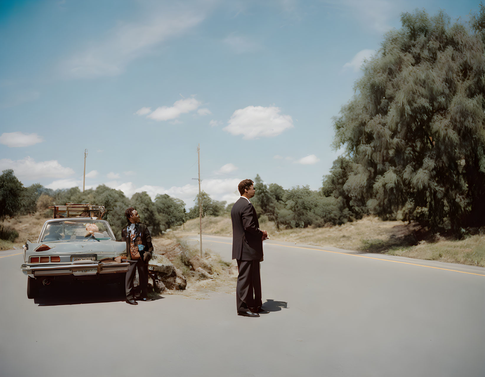 Vintage car photo: Two people on rural road with lush greenery