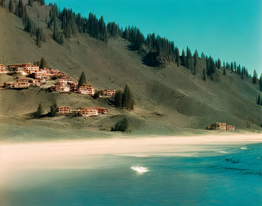 Winter scene: snow-covered shoreline, calm water, rustic buildings, evergreen trees.