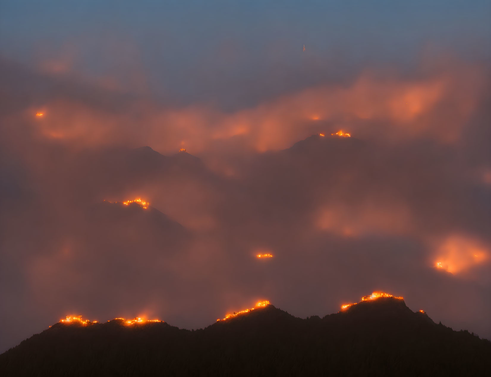 Mysterious orange glow illuminates mountain peaks through dense clouds