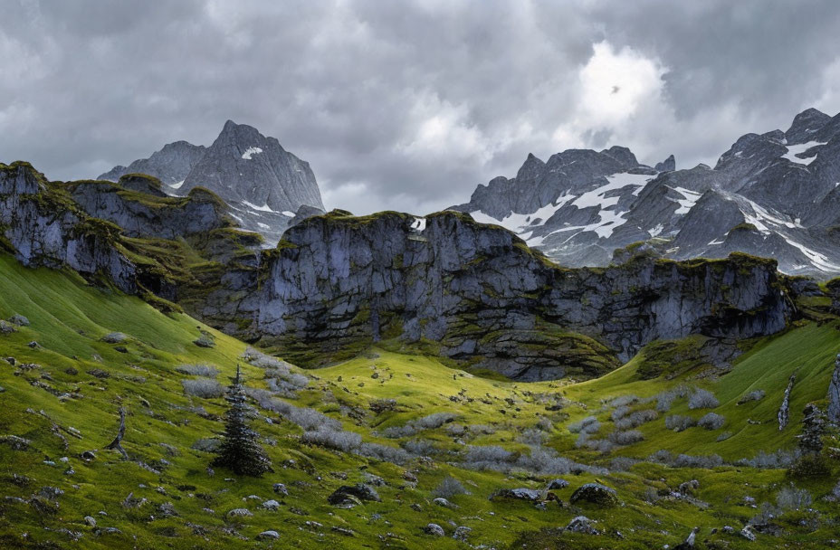 Scenic green valley with rocky outcrops, snow-capped peaks, and dramatic sky