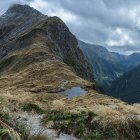 Serene sunrise mountain landscape with people, goats, lush greenery, and blooming flowers