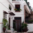 Traditional cobblestone alley with white stone houses, wooden doors, potted plants, and staircase.