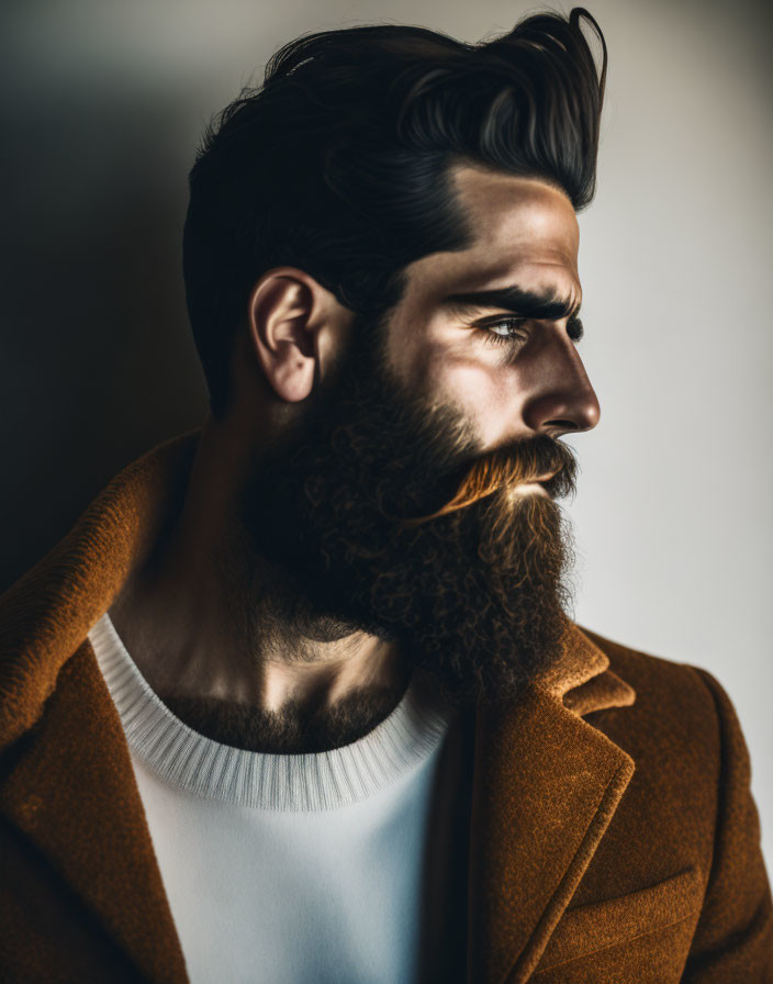 Man with Prominent Beard and Mustache in White Tee and Brown Coat on Neutral Background