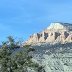 Lush valley with quaint houses, pine tree, and cliffs under clear blue sky