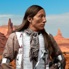 Native American man in traditional attire against blue sky and grasslands