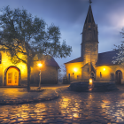 Misty evening scene with cobblestone path, old church, trees, and lamppost