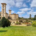 Grand mansion with tower in manicured garden under cloudy sky