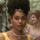 Portrait of two women: one with ornate crown and yellow dress, another blurred amidst flowers.