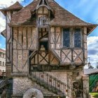 Medieval stone house with timber framing, flowers, plants on cobblestone street.