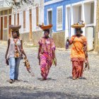 Three young girls in floral dresses stroll down cobbled street with scattered blossoms