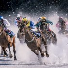 Three jockeys on galloping horses at a racetrack under dramatic sky