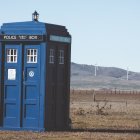 Blue British police box in rural landscape with rolling hills and cloudy sky.