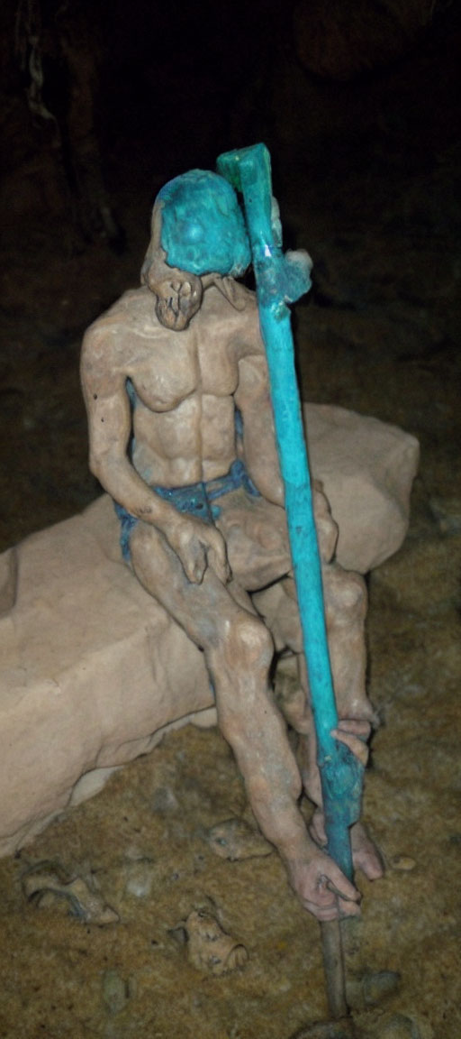 Muscular seated humanoid sculpture with staff in cave setting