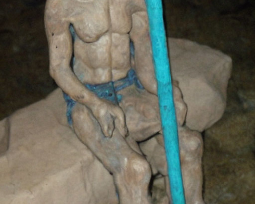 Muscular seated humanoid sculpture with staff in cave setting